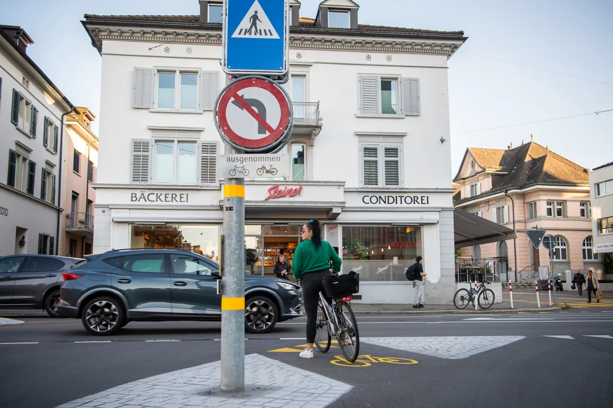 Eine Velofahrerin steht an einer Kreuzung, während ein Auto passiert.